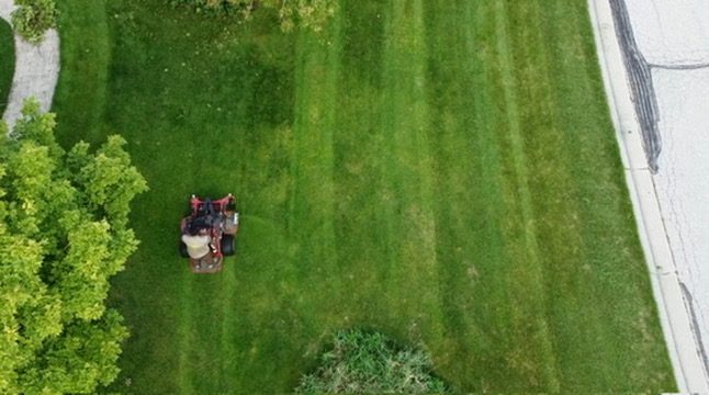 Overhead view of a zero-turn mower cutting clean stripes into a residential lawn